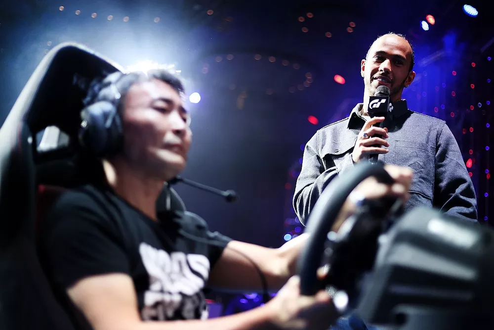Formula 1 Driver, Lewis Hamilton looks on as producer of Gran Turismo, Kazunori Yamauchi gives a demonstration