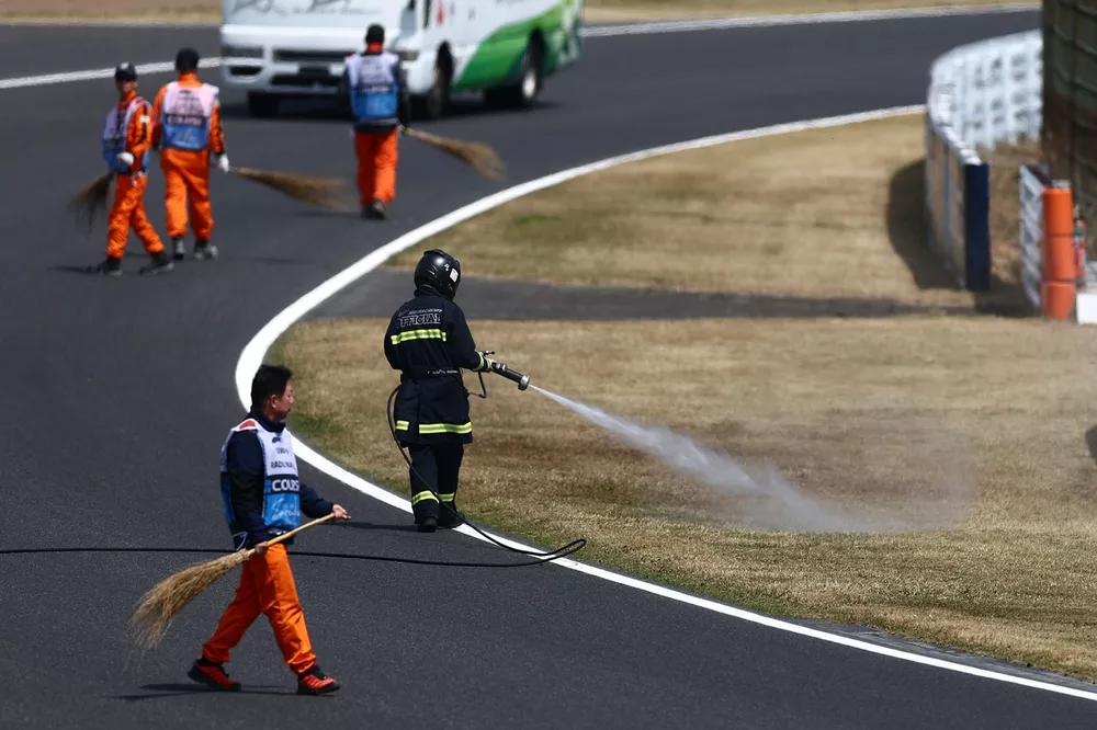 A fire fighter sprays the grass at the side of the track to dampen it after fires during final practice