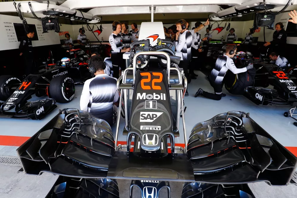A nose cone in front of the McLaren garage. Jenson Button and Fernando Alonso wait in their McLaren MP4-31 Honda cars