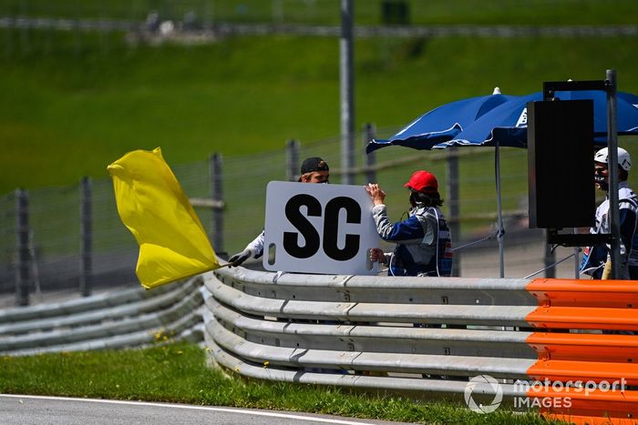 Los oficiales de pista agitan una bandera amarilla y muestran el tablero del coche de seguridad