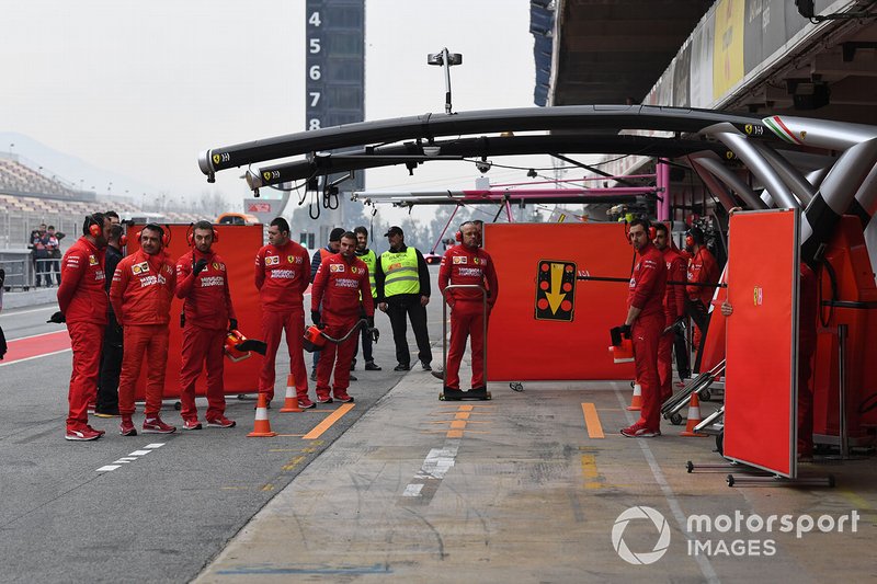 The Ferrari team wait for the return of their car in the pit lane