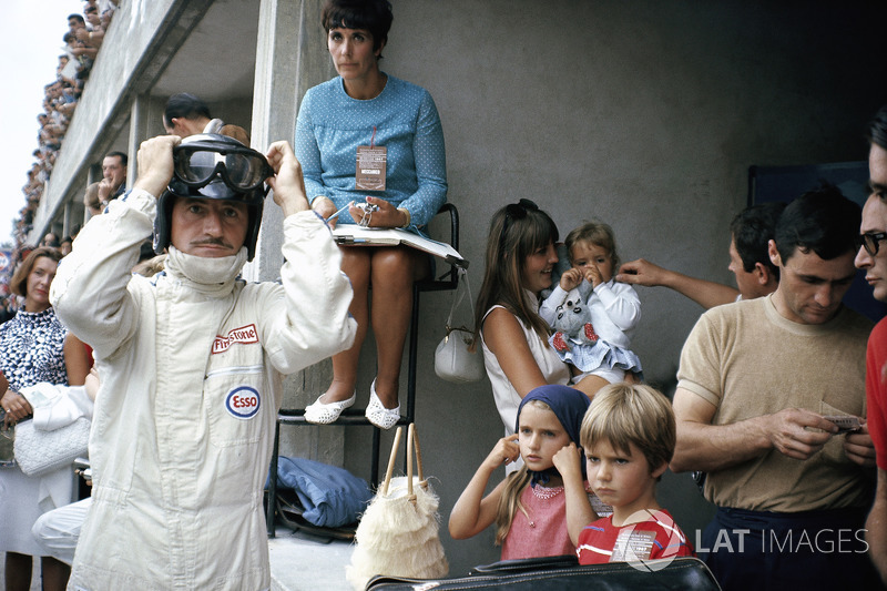 Graham Hill prepares for racing in pits, surrounded by his family: his wife Bette Hill and a nanny w
