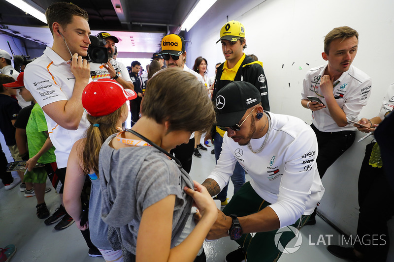 Lewis Hamilton, Mercedes AMG F1, signs a grid kid's short, as Carlos Sainz Jr., Renault Sport F1 Tea