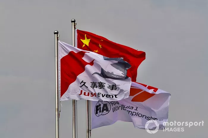 Una bandera china junto a una bandera de Fórmula 1 de la FIA y una bandera de evento de Juss.