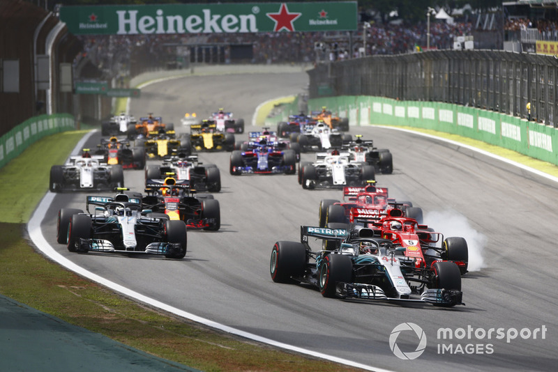 Lewis Hamilton, Mercedes AMG F1 W09, leads a locked-up Sebastian Vettel, Ferrari SF71H, Valtteri Bottas, Mercedes AMG F1 W09, Kimi Raikkonen, Ferrari SF71H, Max Verstappen, Red Bull Racing RB14 Tag Heuer, and the rest of the field at the start.