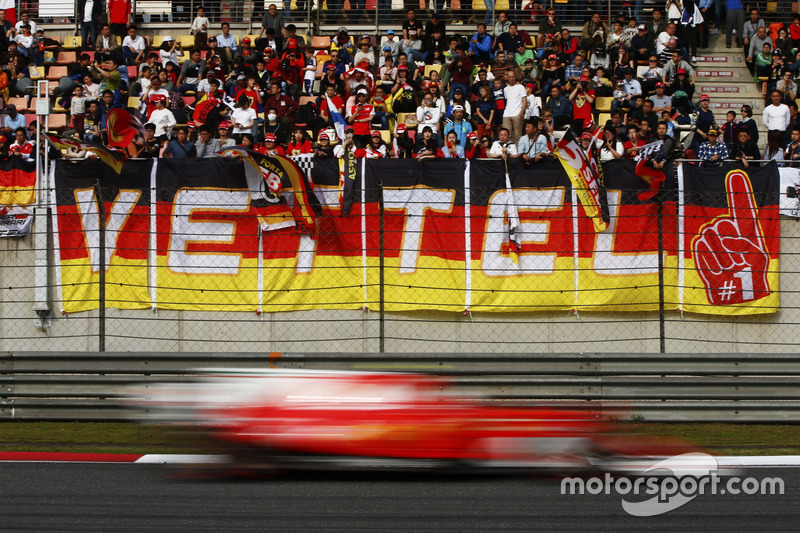 A Ferrari flashes by a stand containing a large number of Sebastian Vettel, Ferrari, fans